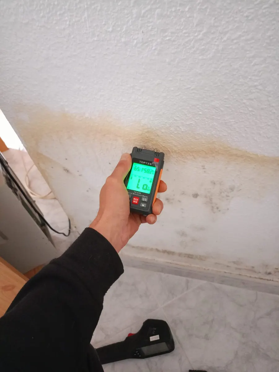 Medidor de humedad apoyado en una pared con mancha de humedad